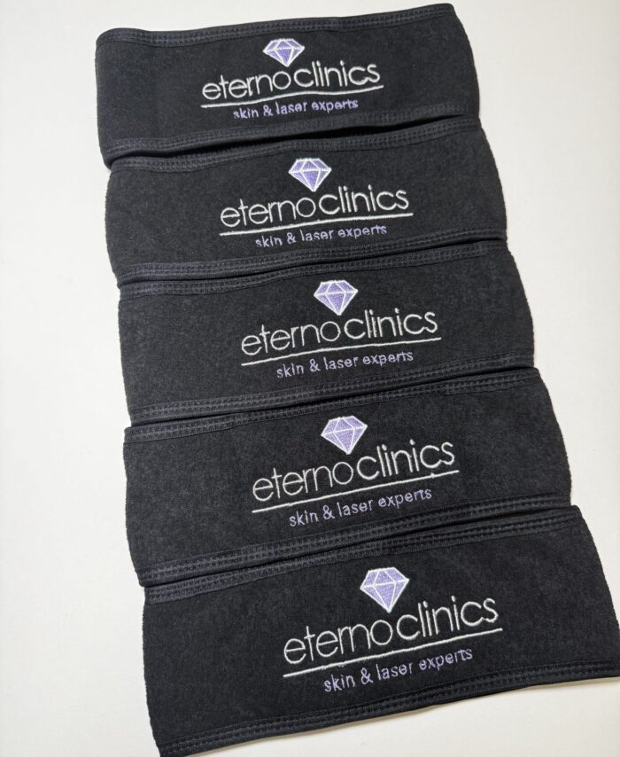 Black spa headbands embroidered with clinic logo in white thread, stacked neatly to show professional beauty salon branding for skincare and laser treatments.