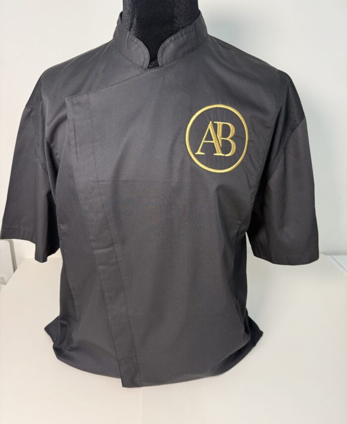 Black short sleeve unisex chef jacket with gold embroidered AB logo on chest, modern mandarin collar professional kitchen uniform
